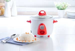 A small white and red rice cooker sitting on a counter beside a dish of prepared white rice.
