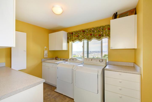 a room with yellow walls and white washer, dryer, and cabinets