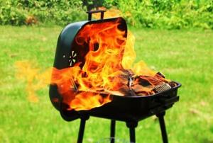 A portable barbeque outdoors with the large flames of a flash fire coming out.