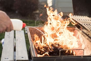 hand applying lighter fluid to bbq grill