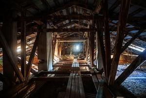 Looking down the length of a long, dark attic with unevenly-spaced floor boards.