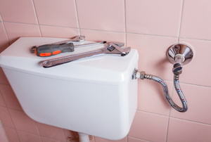 Tools on a toilet tank against a pink tiled wall