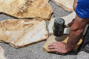 A DIYer working with a mallet and pavers.