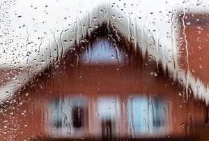 A window looking out on a house with rain pouring down.