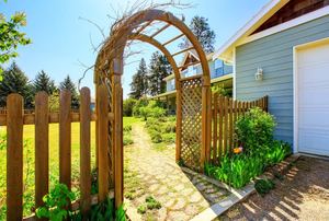 A wood arbor next to a driveway.