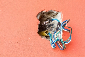 A hole in a wall with wires where an electrical outlet would be.