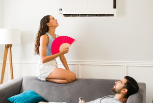 woman with fan looking at AC in wall