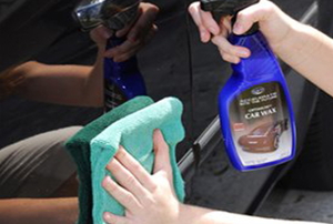 A rag and a bottle of car wax being used to buff a car's exterior.