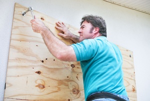 A man uses plywood to board up a window.