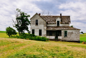 An old fixer upper house in the middle of a field.