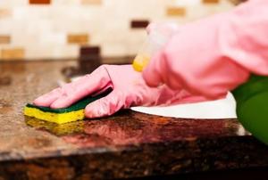 A close-up of gloved hands cleaning a granite countertop.