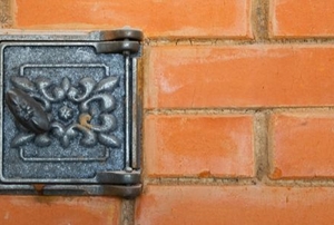 metal flue vent with floral design in brick wall