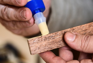 Glue oozing from a tube onto a wood surface.