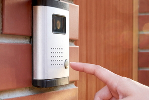 A finger ringing a doorbell that has a camera