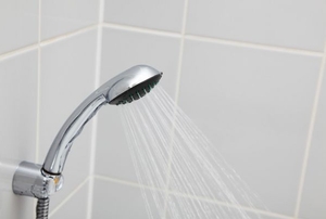Shower faucet pouring water into a shower stall with light grey tiles.