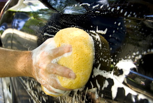 A yellow sponge washing a black car with lots of bubbles. 