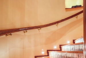 A lit, curved stairway with a handrail mounted on the wall.