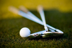 Two golf clubs lying next to a golf ball on green grass.