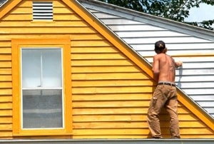 a man paints the outside of the second story of a house yellow