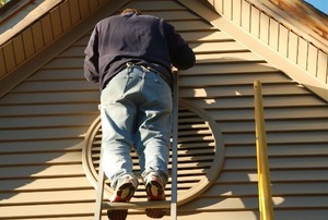 A homeowner on a ladder, painting his vinyl siding.