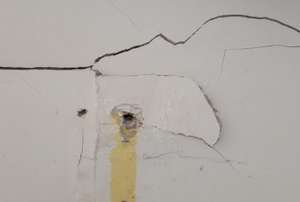 A crack and hole in drywall that needs to be repaired.