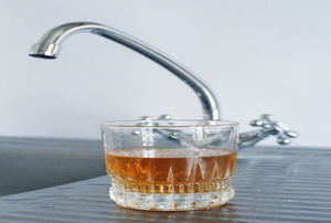 reddish-brown water in a glass on the counter next to the sink
