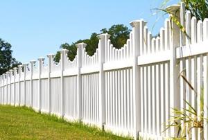 A white picket fence running across a yard on a bright summer's day, with blue sky and trees in the background