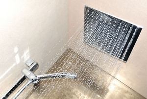 A ceiling mount shower head spraying water down.