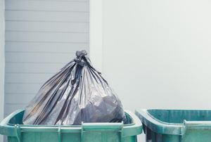 A couple of green trash cans with a black trash bag in one.