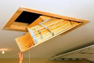 A hand pulling down an access ladder from a garage ceiling.