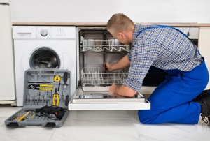 A man works on a dishwasher.