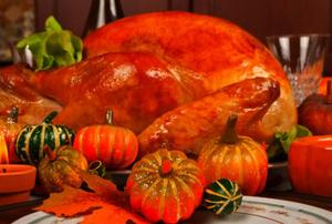 A Thanksgiving turkey with decorative mini-pumpkins in the foreground.