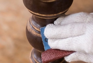 gloved hand removing wood finish with abrasive paper