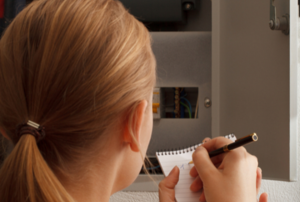 woman taking notes while looking at a fuse box