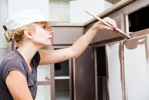 A woman painting kitchen cabinets.