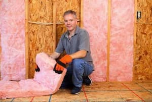 A man installing strips of pink insulation in an attic.