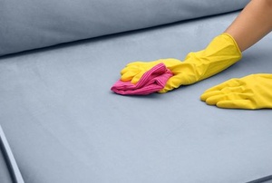 A woman cleans a stain on a couch.