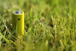 A small, yellow rechargeable battery sitting upright in the grass.
