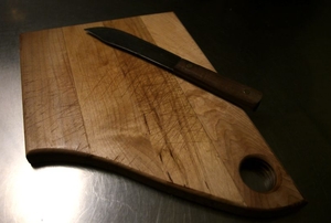 A wooden cutting board on a dark counter with a small knife sitting on top.