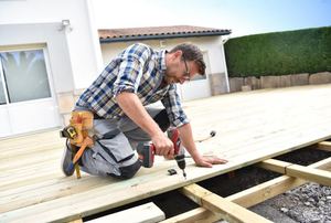 A handyman constructing a wood deck and using an impact driver.