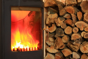 A wood burning stove with a stack of wood beside it.