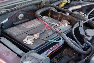 A car battery still connected to the engine under the hood.