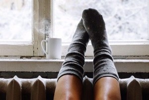 feet with socks on a radiator next to a winter window and hot drink