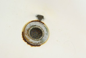 An old sink drain with rust around the metal fitting.