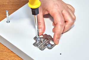 a hand with a screwdriver removing hardware from a piece of wood