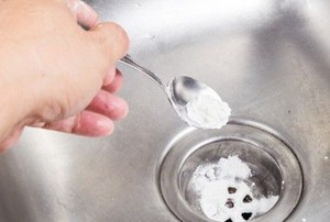 a hand using a spoon to pour powder into a sink drain