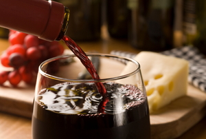 Filling a wine glass with red wine, cheese and grapes sitting in the background.