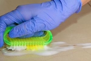 Gloved hand scrubbing tile grout