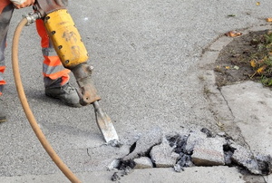person in protective gear using a jackhammer to remove a concrete walkway