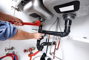 A man works on plumbing under a sink.